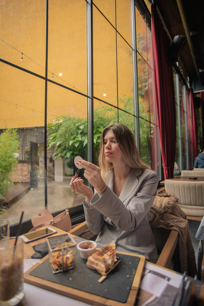 Incredibile e attraente ragazza sta fissando il suo make up nel ristorante dopo aver mangiato - Foto, immagini