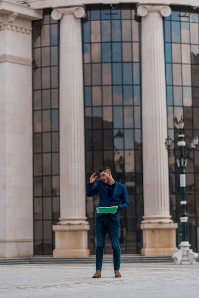 Young manager holding green folder while talking on cellphone on city square - Фото, зображення