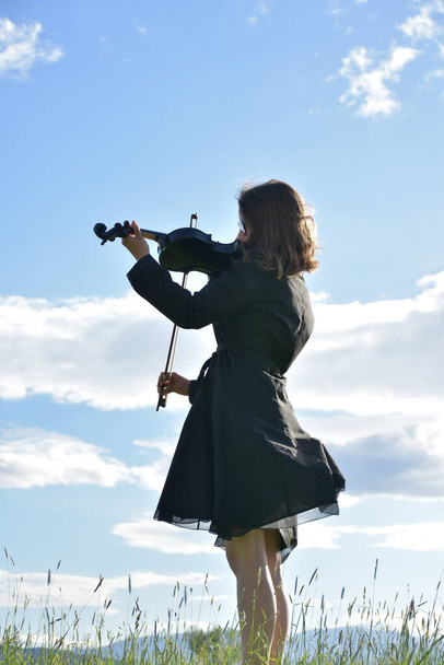 ένα κορίτσι με μαύρο φόρεμα με μαύρο βιολί, - Φωτογραφία, εικόνα