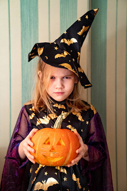 a little girl in a masquerade witch costume with a pumpkin lantern for Halloween - Foto, immagini