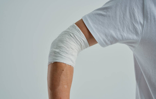 Пациент мужчина в белой футболке с перевязанной рукой на изолированном фоне. Высокое качество фото - Фото, изображение