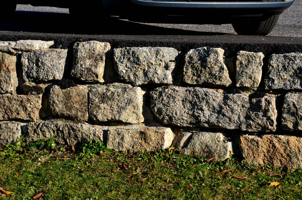 stone retaining wall connected by cement from large stone blocks. there is an asphalt layer on the litter where vehicles are parked. lawn - Photo, Image