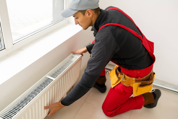 Workman riscaldamento dell'acqua di montaggio radiatore vicino alla finestra nel bianco rinnovato soggiorno, Immagine con spazio copia - Foto, immagini