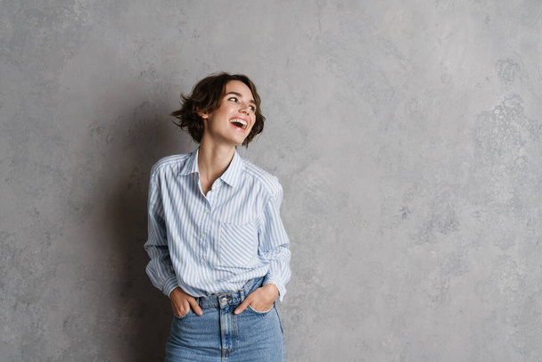 Young brunette woman wearing shirt laughing and looking aside isolated over grey wall - Fotografie, Obrázek