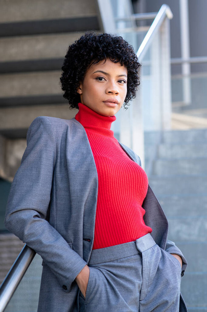A young African-American businesswoman wearing a red turtleneck and a suit in a business building - Фото, изображение