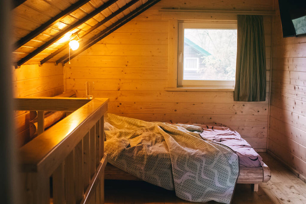 田舎の家の屋根裏部屋の木製の部屋。ダブルベッド、傾斜天井と若い木のトリム。リラクゼーションと楽しい娯楽の概念 - 写真・画像