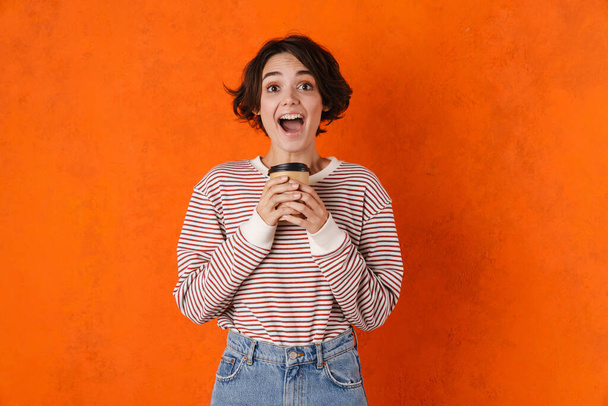 Young brunette woman screaming while drinking coffee isolated over orange wall - Fotografie, Obrázek