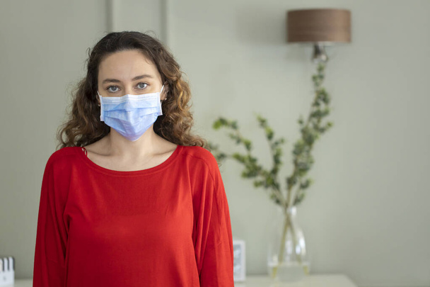 マスクをした若い女性が自宅でコロナウイルスから身を守るために - 写真・画像