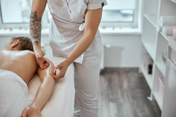 Профессиональный мастер массажа делает процедуры белой женщине в минималистичном современном кабинете - Фото, изображение