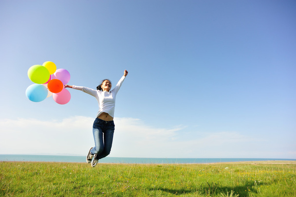 Young asian woman jumping on green grassland with colored balloons - Fotó, kép