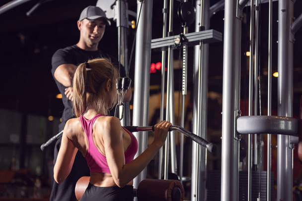 Νεαρή Ασιάτισσα γυναίκα φορώντας ενεργό φθορά άντληση μυών από τη μηχανή άσκησης, ενώ η άσκηση στο γυμναστήριο. - Φωτογραφία, εικόνα