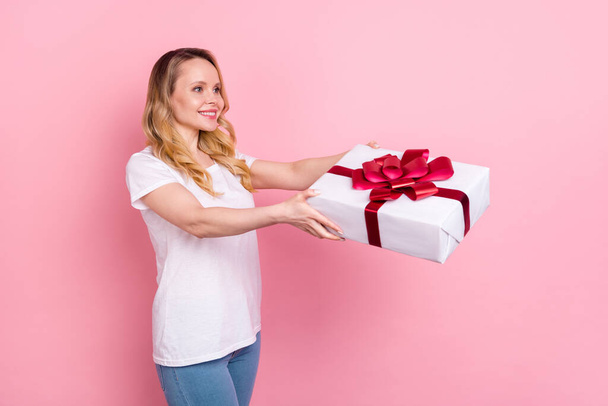 Photo of positive pretty young woman hold hands present box give empty space isolated on pink color background - Foto, immagini