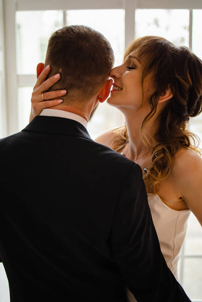 Beautiful wedding couple in bright room. They kiss and hug each other - Fotografie, Obrázek