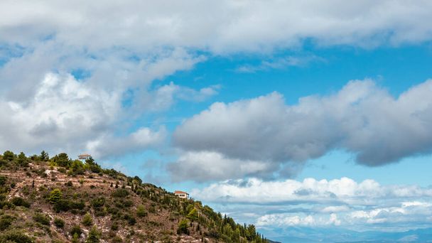 Scenic vibrant landscape with traditional Greek villas on green high hills on blue scenic sky with dramatic cloudscape on Lefkada island, Greece. Travel in summer - Photo, Image