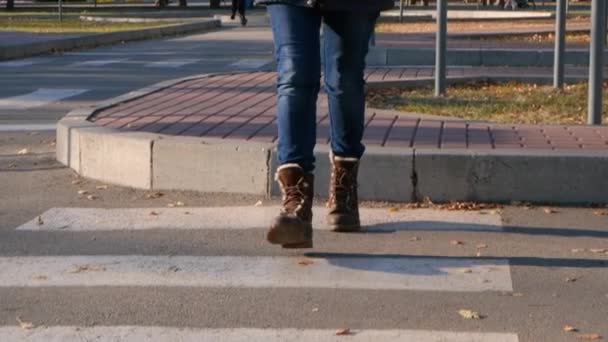 Een vrouw met bruine schoenen steekt de weg over bij een voetgangersovergang, benen van dichtbij. - Video