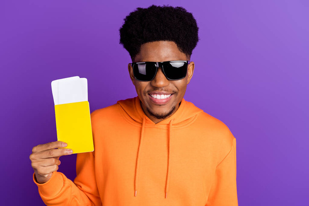 Photo of charming young afro american cool man hold hands tickets vacation trip isolated on violet color background - 写真・画像