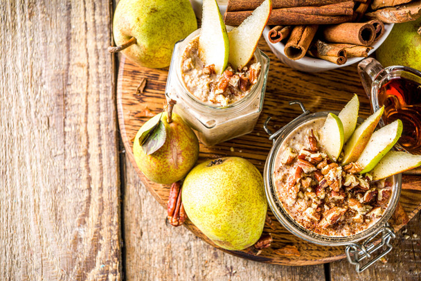 Sweet and spicy autumn breakfast oats recipe, Homemade pear and cinnamon overnight oatmeal with spices and yogurt, wooden background copy space - 写真・画像