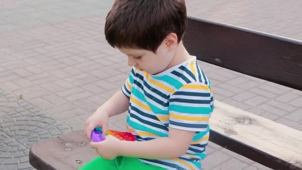 Egy 4 éves gyerek játszik a Pop It-tal a városi parkban. Stresszoldó játék a gyermekek finom motoros készségeinek fejlesztésére. - Felvétel, videó