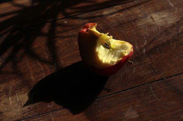 укушенное яблоко, корешок на темном деревянном фоне  - Фото, изображение