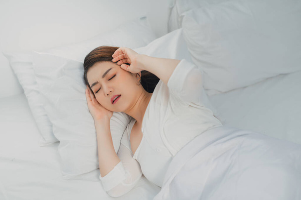 Beautiful young woman suffering from headache while lying in bed - Photo, Image
