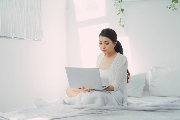 Laptopot használó fiatal nő egy hideg téli napon a hálószobában. - Fotó, kép