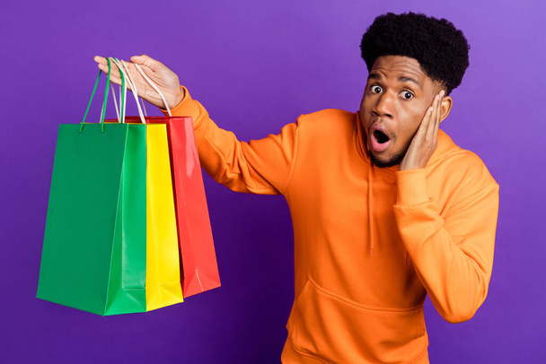 Photo of shocked young dark skin man hold hand cheek bags shop wear sweater isolated on purple color background - Photo, Image
