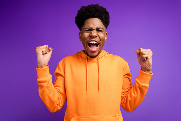 Photo of cheerful young dark skin man winner good mood celebrate champion fists isolated on purple color background - Valokuva, kuva
