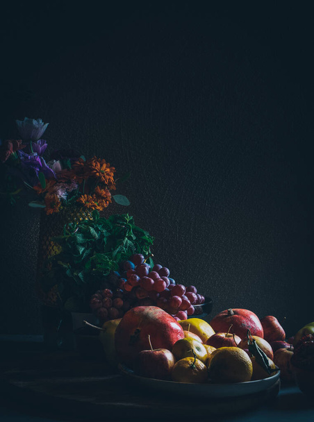 Σκούρο μπαρόκ αναγεννησιακό στυλ νεκρή φύση φωτογραφία φρούτων και λουλουδιών. Μήλα, σταφύλια, ρόδια, κυδώνια, άνθη μέντας και κήπου. - Φωτογραφία, εικόνα