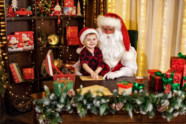 Noel Baba 'yı ziyaret eden küçük çocuk ona Noel mektuplarıyla zarfları açmasında yardım ediyor. Tatil kavramı - Fotoğraf, Görsel