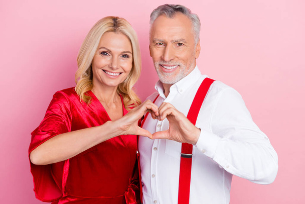 Portrait of two beautiful handsome cheerful spouses hugging showing heart symbol isolated over pink pastel color background - Fotografie, Obrázek