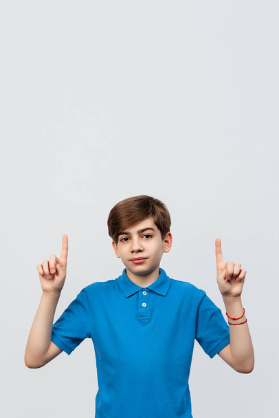 Portret van een charmante jongen van 12-14 jaar oud die naar de camera kijkt terwijl hij zijn handen omhoog steekt en glimlacht. Studio shot, witte achtergrond, geïsoleerd - Foto, afbeelding