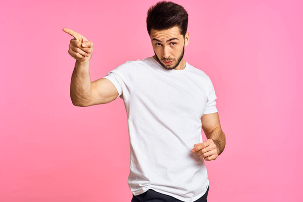 a handsome man in a white t-shirt gesturing with his hands on a pink background - Fotoğraf, Görsel