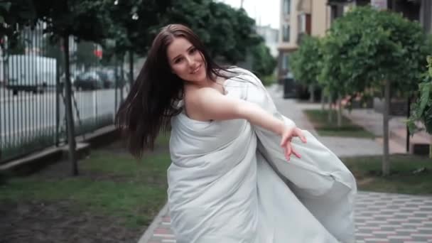 Menina bonita em um cobertor branco andando pela rua. câmara lenta. - Filmagem, Vídeo
