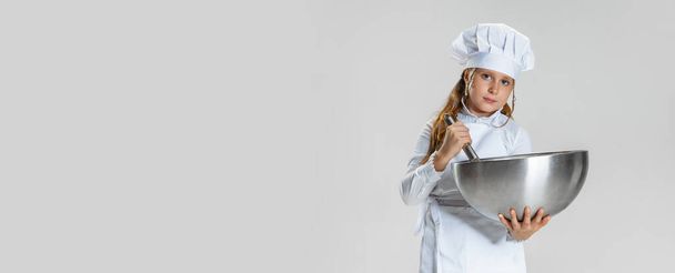 Flyer with little cute girl in white cook uniform and huge chefs hat posing isolated on white studio background. - Foto, imagen