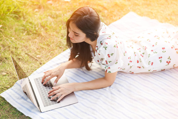beautiful freelance asian women lie about relax and working jobs on laptop in the garden and over sunlight background work from home concept - 写真・画像