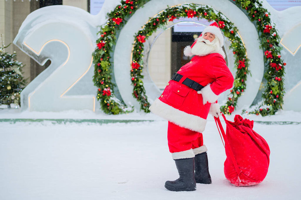 Santa Claus posing with a bag of gifts on the background of Christmas decorations outdoors - Fotoğraf, Görsel