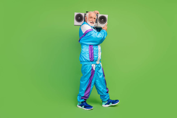 Photo of pretty charming senior man wear sportive suit listening boombox smiling isolated green color background - Photo, Image