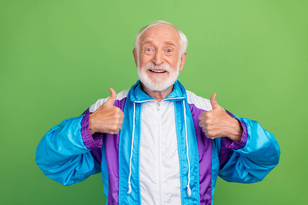 Photo of sweet charming senior man wear sportive suit smiling showing thumbs up isolated green color background - Foto, immagini