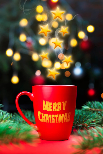 Christmas stars bursting from Coffee mug on the red surface table with Christmas tree lights and spruce branches in the background - Foto, Imagen