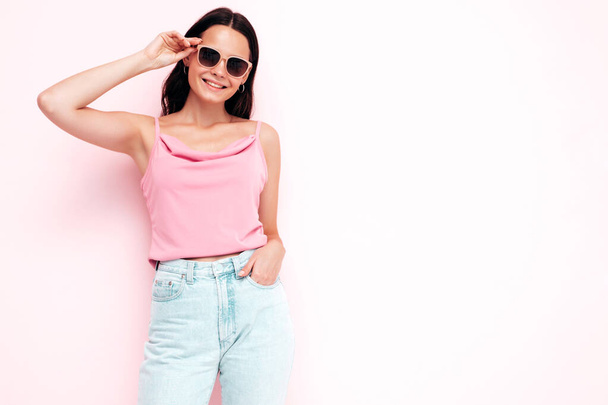Closeup portrait of young beautiful smiling female in trendy summer clothes. Sexy carefree woman posing near pink wall in studio. Positive model having fun indoors. Taking off sunglasses - Fotó, kép