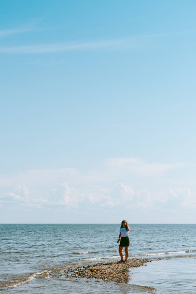 Mujer con el pelo largo y rizado marrón caminando por la costa del mar Báltico en la península de Sorve en Saaremaa, Estonia durante el día soleado y tranquilo - Foto, imagen