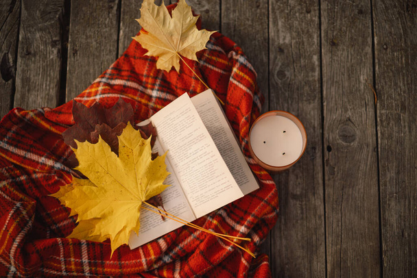 Nyílt könyv gyertyával és csokor őszi levelek egy kockás fa háttér - Fotó, kép