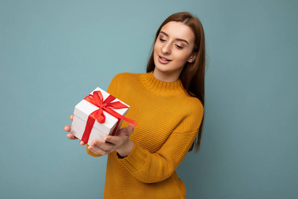 Shot of attractive positive smiling young brunette woman isolated over colourful background wall wearing everyday trendy outfit holding gift box and looking to the side - Foto, immagini