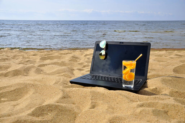 Remote work, a black laptop and sunglasses on a sandy beach. - Foto, imagen