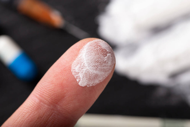 Human finger in cocaine or other drug. In the background are tablets, a syringe, money, drugs. Selective focus. - Foto, immagini