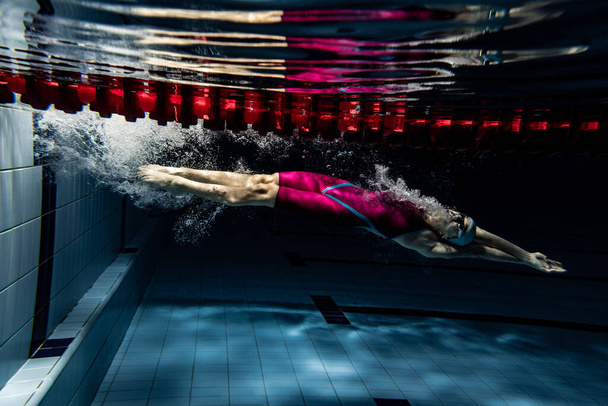 Underwater shooting. One female swimmer training at pool, indoors. Underwater view of swimming movements details. - Foto, imagen