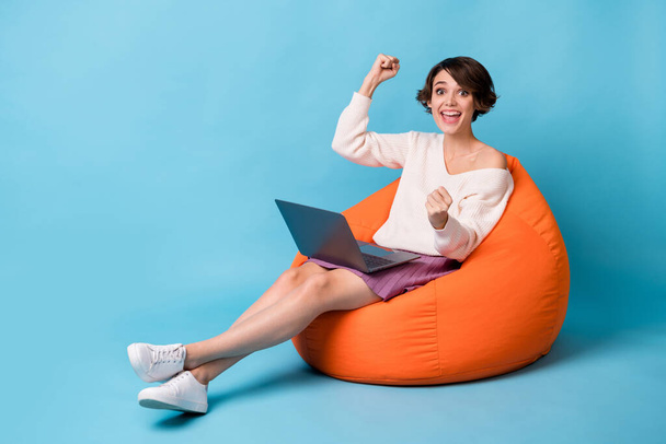Full length photo portrait of cheerful woman with laptop sitting in orange beanbag isolated on pastel blue colored background - Fotoğraf, Görsel