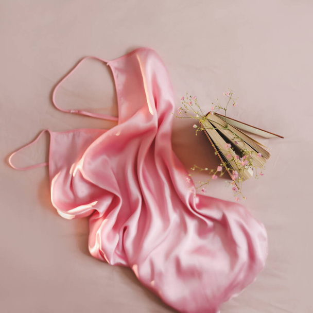 Beauty and fashion blog concept. Stylish feminine accessories flatlay top view. Woman pink silk dress and a book - Фото, изображение