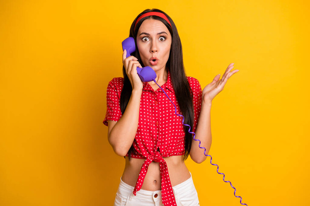 Photo of sweet shocked young girl dressed red shirt communicating vintage phone isolated yellow color background - Photo, image