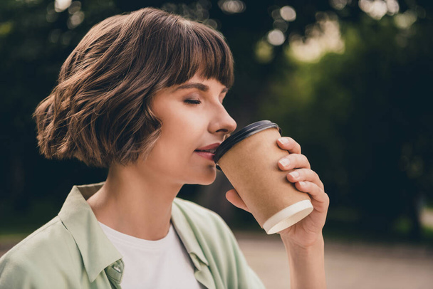 Profile side view portrait of attractive dreamy girl drinking hot sweet latte beverage resting on fresh air outdoors - 写真・画像
